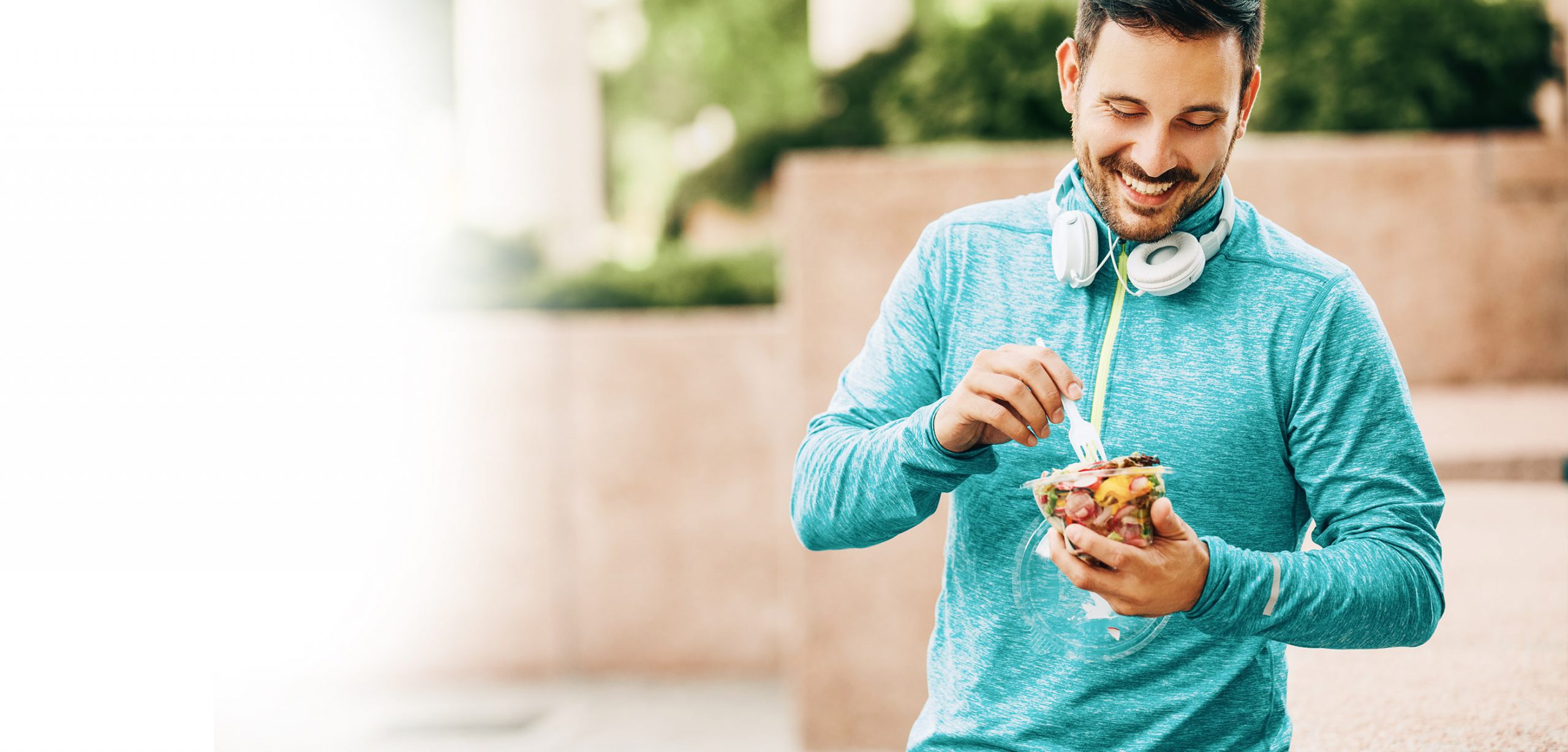 Man with headphones around his neck enjoying a healthy meal after working out.